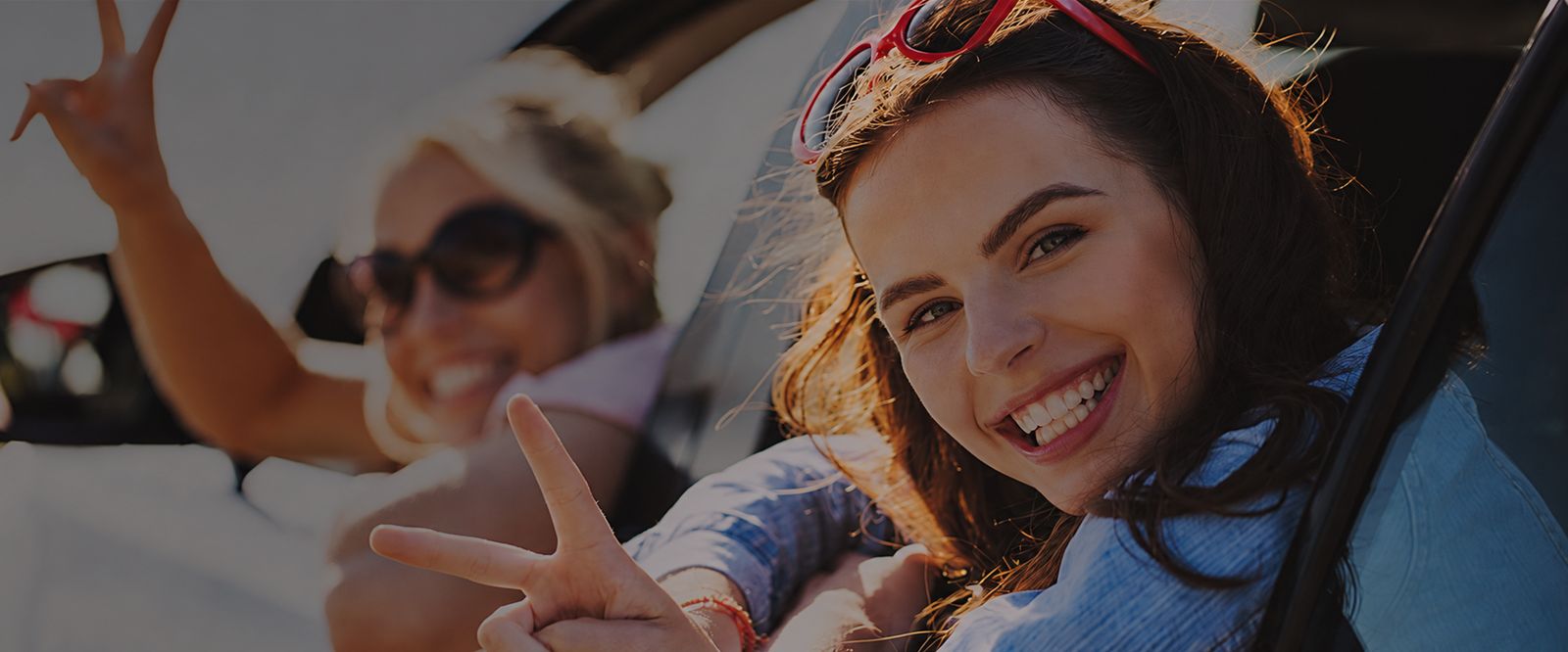 Two smiling learners waving from the windows of a car